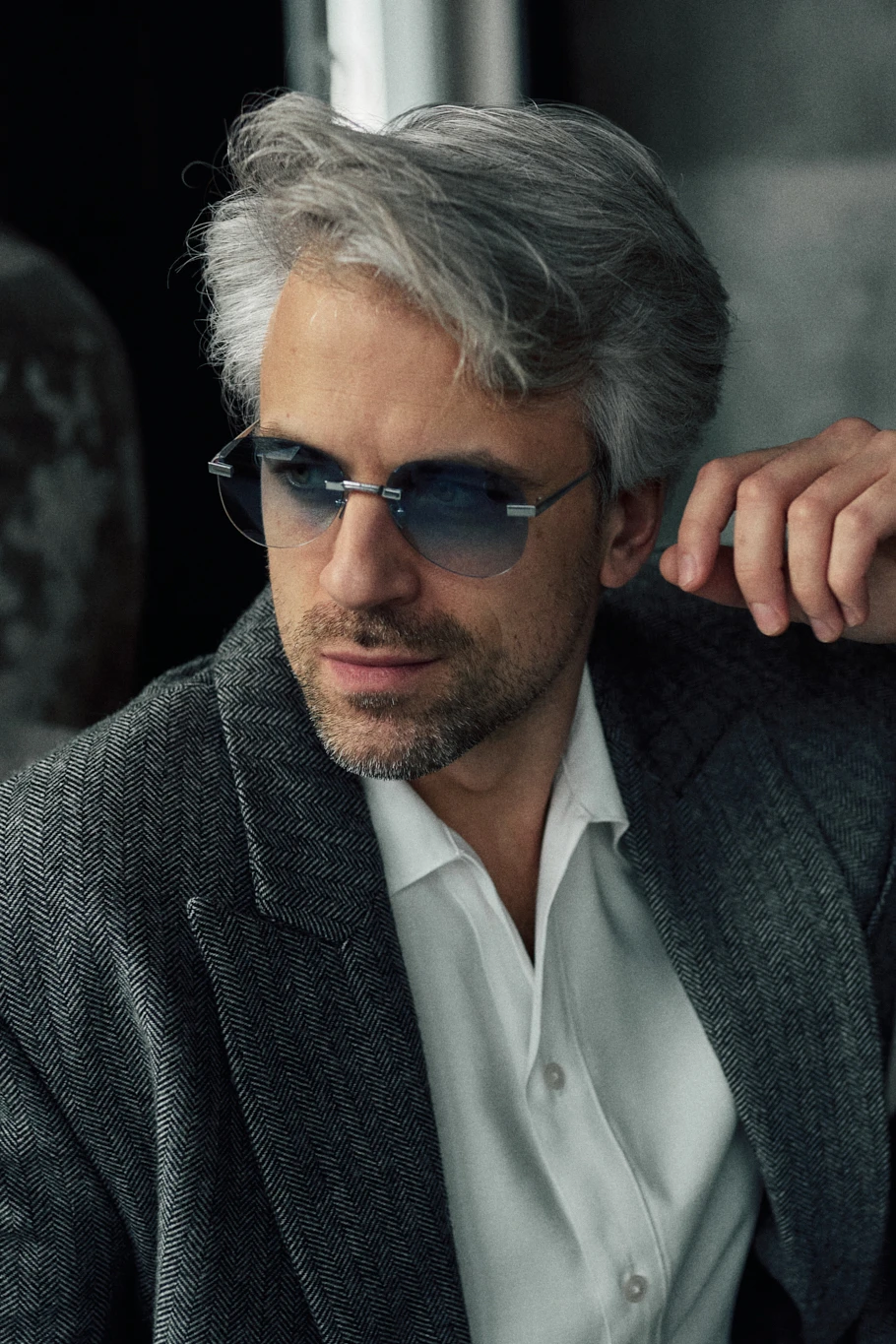 Man in a herringbone jacket and white shirt wearing PTERON Azure silver aviator sunglasses with blue lenses