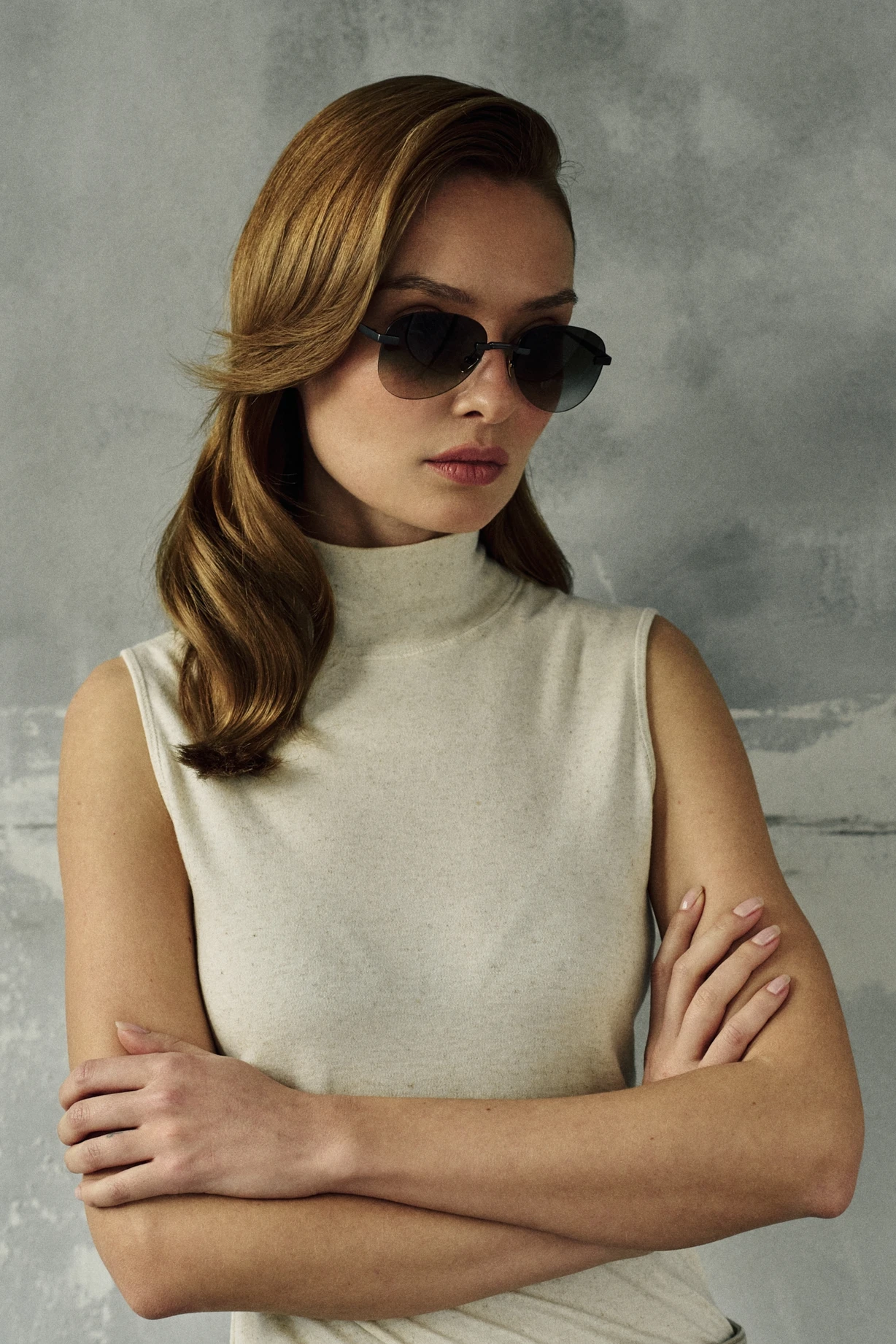 Woman with crossed arms wearing PTERON Hunter dark titanium aviator sunglasses with green gradient lenses